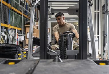 A forklift moving goods between tall warehouse shelves