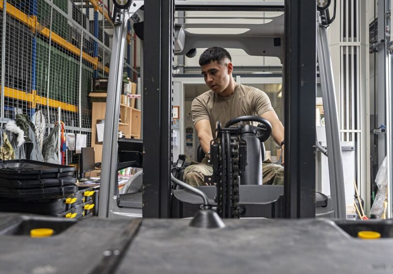 A forklift moving goods between tall warehouse shelves